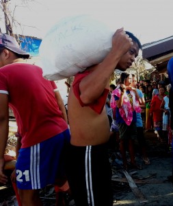 A survivor of Typhoon Yolanda who just received a sack of relief goods. On his back are fellow survivors awaiting for their relief. 