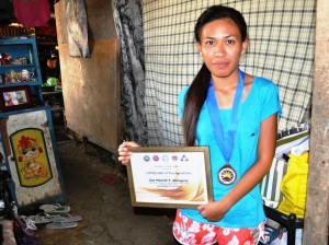 Gay Myrell Abrogena, one of the first Student Grants in Aide Program for Poverty Alleviation (SGPPA) graduate from Pinili, Ilocos Norte shows her awards as one of the exemplary SGPPA scholars in the country.